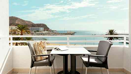 Näkymä parvekkeelta, jossa on pöytä ja tuolit, kohti rantaa ja merta. (Tekoälyn luoma teksti)