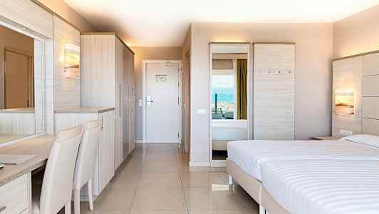 Modernisti sisustettu hotellihuone, jossa on parivuode, vaatekaappi ja kirjoituspöytä, näkymä merelle. (Tekoälyn luoma teksti)