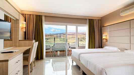 Hotellihuone, jossa kaksi yhden hengen sänkyä, kirjoituspöytä ja näkymä maisemaan lasioven kautta. (Tekoälyn luoma teksti)