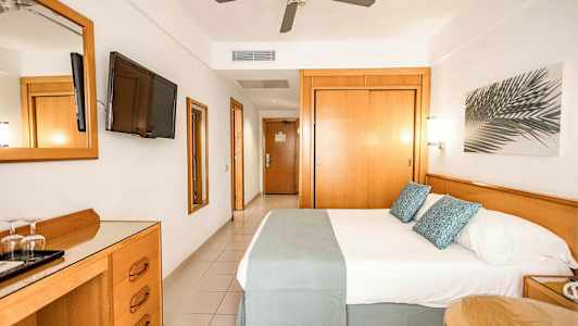 Hotellihuone, jossa on parivuode, seinälle kiinnitetty televisio, kattotuuletin ja puukalusteet. (Tekoälyn luoma teksti)