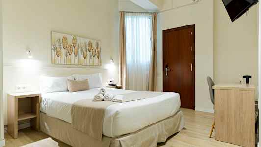 Valoisa hotellihuone, jossa on parivuode, työpöytä ja seinälle kiinnitetty televisio. (Tekoälyn luoma teksti)