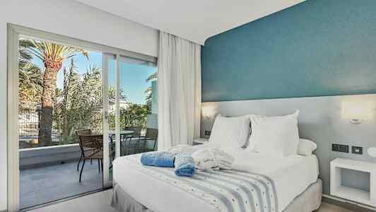 Makuuhuone parivuoteella, valkoiset vuodevaatteet sekä sininen koristeellinen seinä, parveke, jossa tuolit ja näkymä palmuihin. (Tekoälyn luoma teksti)