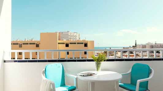 Parveke, jossa on kaksi tuolia, pöytä ja näkymä rakennuksille ja merelle. (Tekoälyn luoma teksti)