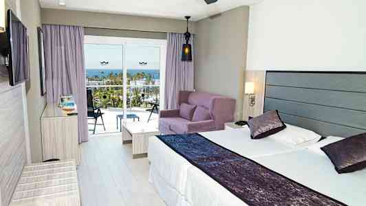 Moderni hotellihuone, jossa on parivuode, sohvaryhmä ja parveke merinäköalalla. (Tekoälyn luoma teksti)