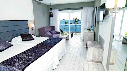 Hotellihuone, jossa on parivuode, sohva ja merinäköala suurten ikkunoiden takana. (Tekoälyn luoma teksti)