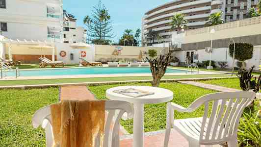 Ulkouima-allas, jota ympäröivät viheralueet ja aurinkotuolit, taustalla valkoisia rakennuksia. (Tekoälyn luoma teksti)