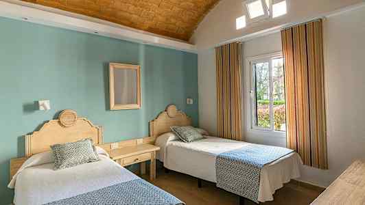 Kaksi yksittäissänkyä, joissa puiset päätylaudat, hotellihuoneessa, jossa on vihreä seinä ja ikkuna. (Tekoälyn luoma teksti)