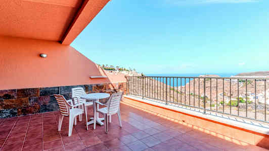 Terassi, jolla on pöytä, tuolit ja kaide sekä merinäköala. (Tekoälyn luoma teksti)