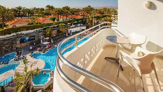 Näkymä parvekkeelta, jossa on pöytä ja tuolit, kohti uima-allasta ja palmuja. (Tekoälyn luoma teksti)