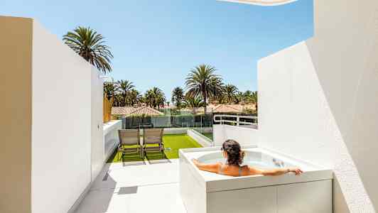 Henkilö istuu porealtaassa terassilla, josta on näkymä palmuihin ja taloihin. (Tekoälyn luoma teksti)