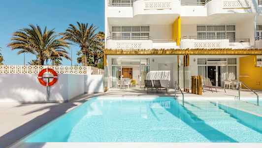 Ulkouima-allas hotellissa, jossa on valkoiset ja keltaiset julkisivut, ympärillä palmuja. (Tekoälyn luoma teksti)