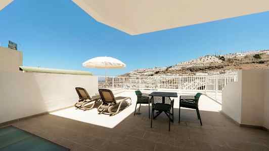 Terasilla aurinkotuoleja, varjo ja ulkokalusteet, näkymä aurinkoon ja mäenrinteeseen. (Tekoälyn luoma teksti)