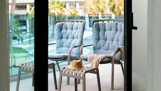 Kaksi sinistä istuintuolia ja yksi jakkara, jossa hattu parvekkeella. (Tekoälyn luoma teksti)