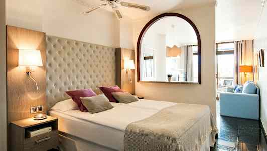 Kahden hengen huone, jossa leveä sänky, valaisimet ja koristeellisia tyynyjä. (Tekoälyn luoma teksti)