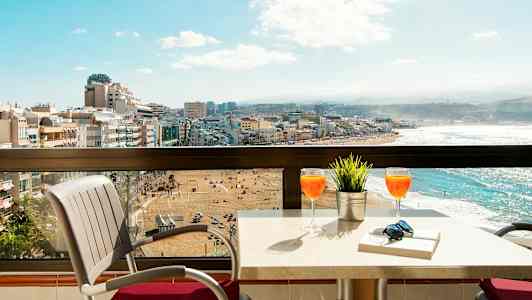 Parveke, jossa pöytä ja tuolit, näkymä rannalle ja kaupunkiin. (Tekoälyn luoma teksti)