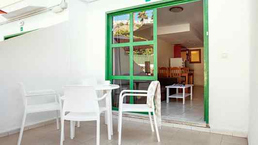 Ulkoterassi, jossa valkoisia kalusteita ja vihreä oviranainen, joka johtaa asuntoon. (Tekoälyn luoma teksti)