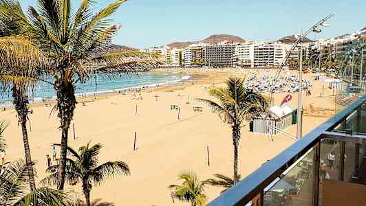 Näkymä leveälle hiekkarannalle, jossa palmuja ja kaupungin rakennuksia taustalla. (Tekoälyn luoma teksti)