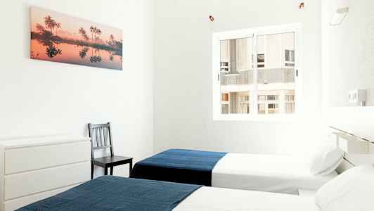 Kaksi yhden hengen sänkyä valoisassa huoneessa, jokaisessa sininen peitto. (Tekoälyn luoma teksti)