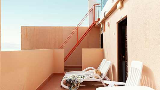 Yksityinen terassi, jossa aurinkotuoleja, viltti ja laukku. (Tekoälyn luoma teksti)