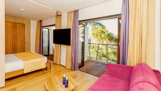 Hotellihuone, jossa sänky, vaaleanpunainen sohva, televisio ja parveke. (Tekoälyn luoma teksti)