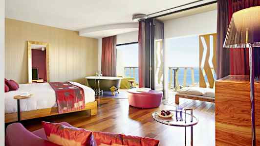 Hotellihuone, jossa sänky, kylpyamme, istuinalue ja näkymä merelle. (Tekoälyn luoma teksti)