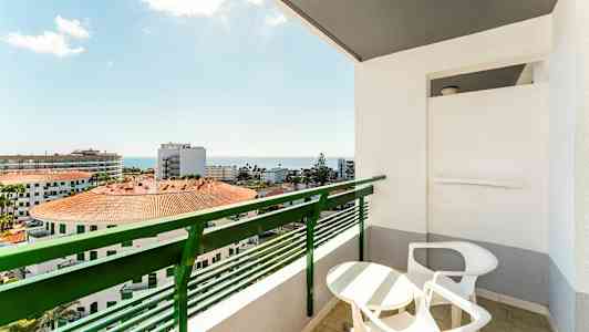 Parveke, jossa pöytä ja tuolit, sekä näkymä rakennuksiin ja merelle. (Tekoälyn luoma teksti)