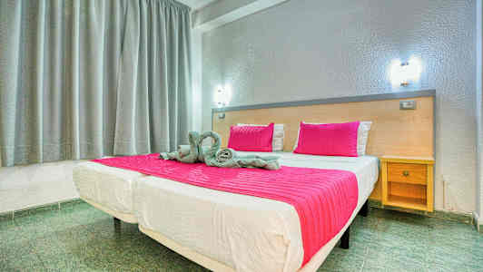 Sänky, jossa on vaaleanpunainen peitto ja tyynyjä, huoneessa, jossa on harmaat verhot ja puupenkki. (Tekoälyn luoma teksti)