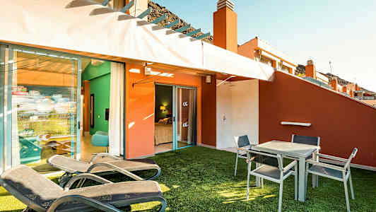 Terassi, jossa on aurinkotuoleja, pöytä ja tuoleja sekä näkymä makuuhuoneeseen. (Tekoälyn luoma teksti)