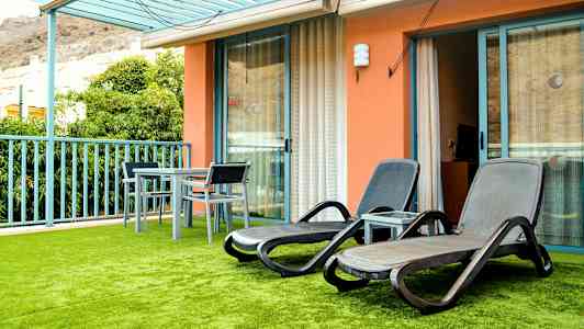 Terassi, jossa aurinkotuoleja ja pöytä tuoleineen, sekä vihreä keinotekoinen nurmikko. (Tekoälyn luoma teksti)