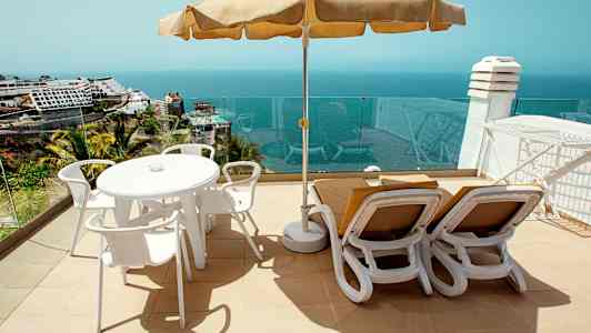 Aurinkoterassi, jossa pöytä, tuolit ja aurinkotuolit sekä merinäköala. (Tekoälyn luoma teksti)