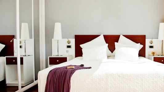 Hotellihuone, jossa on parivuode, valkoiset vuodevaatteet ja tyynyt sekä peitto verhottuna huovalla. (Tekoälyn luoma teksti)