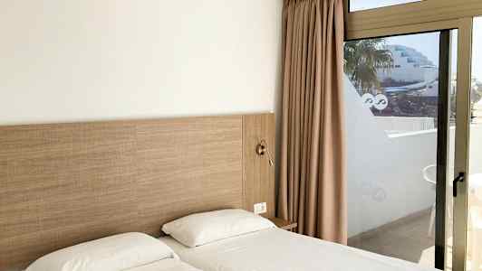 Kaksi yhden hengen sänkyä valkoisilla lakanoilla lasioven vieressä näkymällä. (Tekoälyn luoma teksti)