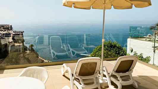 Kaksi aurinkotuolia ja aurinkovarjo terassilla, näkymä merelle. (Tekoälyn luoma teksti)