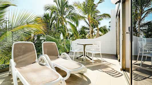 Aurinkotuolit ja ruokapöytä terassilla, näkymä palmupuihin. (Tekoälyn luoma teksti)