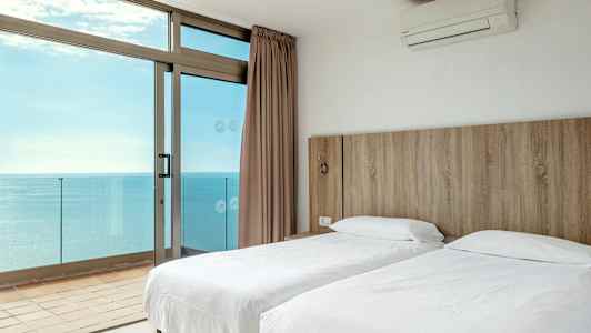 Hotellihuone, jossa on kaksi erillistä sänkyä ja näkymä merelle suurista ikkunoista. (Tekoälyn luoma teksti)