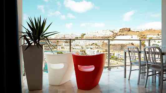 Parveke, josta näkymä kaupunkiin ja vuorille, kaksi modernia tuolia ja ruukkukasvi. (Tekoälyn luoma teksti)