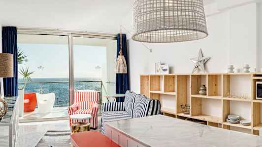 Näkymä nykyaikaiseen olohuoneeseen merihenkisellä sisustuksella, meri näkyy lasiovien läpi. (Tekoälyn luoma teksti)