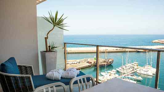 Näkymä satamaan, jossa on useita veneitä, parvekkeelta, jolla on tuoleja ja ruukkukasvi. (Tekoälyn luoma teksti)