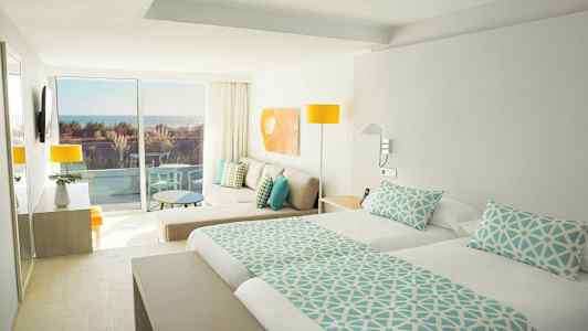 Vaalea hotellihuone parivuoteella, istuinalueella ja parvekkeella merinäköalalla. (Tekoälyn luoma teksti)