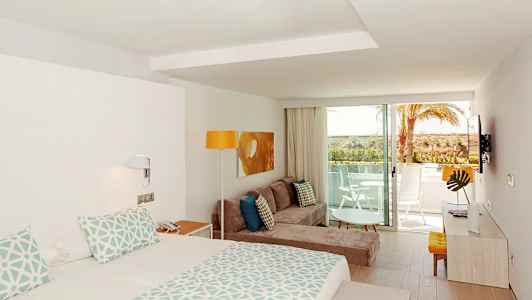 Moderni hotellihuone, jossa sänky, sohva, koristeellinen pöytä ja parveke kauniilla näkymällä. (Tekoälyn luoma teksti)