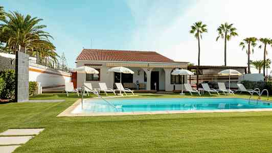 Huvila, jossa uima-allas ja aurinkotuoleja, ympärillä nurmikkoa ja palmuja. (Tekoälyn luoma teksti)