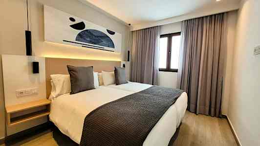 Nykyaikainen hotellihuone, jossa kaksi erillistä vuodetta, taidetta seinällä ja ikkuna verhoineen. (Tekoälyn luoma teksti)