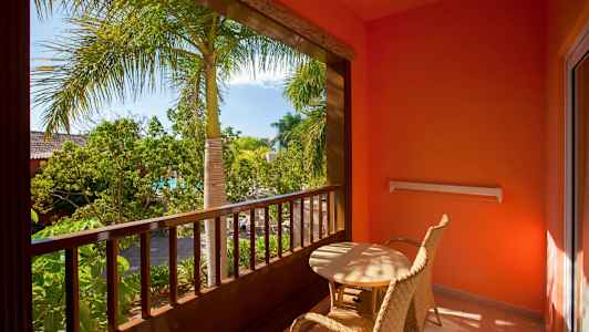 Parveke, jossa kaksi punottua tuolia ja pöytä, ympäröitynä kasveilla ja palmuilla. (Tekoälyn luoma teksti)