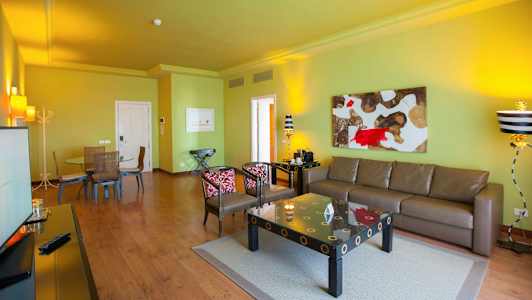 Olohuone, jossa on vihreä seinä, ruskea sohva, taidetta seinällä ja ruokapöytä tuoleineen. (Tekoälyn luoma teksti)