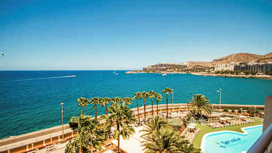 Näkymä uima-altaalle ja palmuihin, taustalla meri ja rakennuksia. (Tekoälyn luoma teksti)