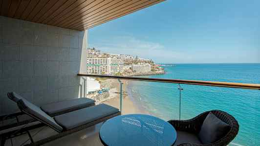 Näkymä parvekkeelta merelle ja rannalle, etualalla pöytä ja tuolit sekä aurinkotuoleja. (Tekoälyn luoma teksti)