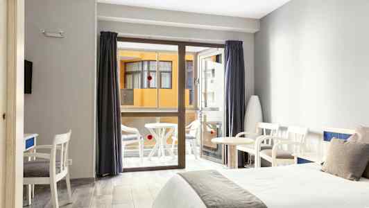 Hotellihuone, jossa on kaksi sänkyä, istuinkalusteet ja parveke taustalla. (Tekoälyn luoma teksti)