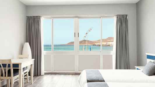 Valoisa hotellihuone, josta on näkymä merelle suuren ikkunan kautta. (Tekoälyn luoma teksti)