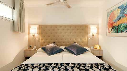 Hotellihuone, jossa on parivuode, pehmustettu sängynpääty, kattotuuletin ja seinävalaisimet. (Tekoälyn luoma teksti)