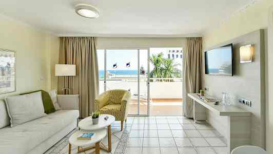 Olohuone, jossa on vaaleat huonekalut ja suuret lasiovet, jotka johtavat parvekkeelle merinäköalalla. (Tekoälyn luoma teksti)